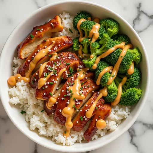Close-up of a sticky chicken rice bowl with glossy sauce, sesame seeds, and vibrant green onions.