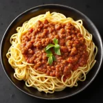 Close-up of a plated homemade spaghetti with meat sauce, garnished with herbs.