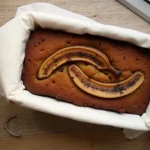 Close-up of a loaf of banana bread made with two ripe bananas, showcasing a golden-brown crust and moist texture.