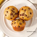 Close-up of a freshly baked eggless banana chocolate chip muffin with a golden crust and chocolate chips on top.