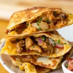 Stack of golden-brown chicken quesadillas on a decorative plate, filled with melted cheese and savory chicken.