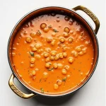 Close up of chickpea curry in a metal pot with brass handles
