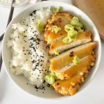 Overhead shot of a bowl of rice topped with chicken and green onions.