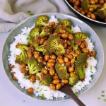 Close-up of garlic broccoli stir fry served over rice in a bowl, with a wooden spoon.