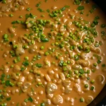 Close up of vegan beef stew in a skillet, topped with chopped green onions.
