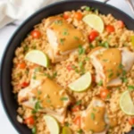 Overhead view of One-Pot Mexican Chicken and Rice in a dark skillet with lime wedges.