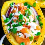 A close-up shot of a Whole30-compliant family meal, featuring roasted spaghetti squash halves filled with seasoned shrimp, garnished with red onions, a creamy sauce, parsley, and green onions.
