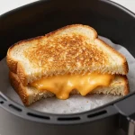 A perfectly golden grilled cheese sandwich made in an air fryer, served on a plate with a side of dipping sauce.