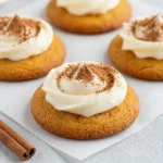 Close-up of pumpkin cookies topped with cinnamon cream cheese frosting on a wooden table.