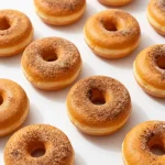 Freshly baked pumpkin donuts topped with cinnamon sugar on a wooden table