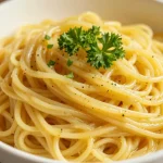 A bowl of garlic butter noodles garnished with parsley and served on a wooden table.