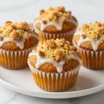 Freshly baked pumpkin muffins topped with creamy maple icing on a rustic wooden table