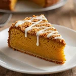 A slice of iced pumpkin coffee cake on a white plate with a fork beside it